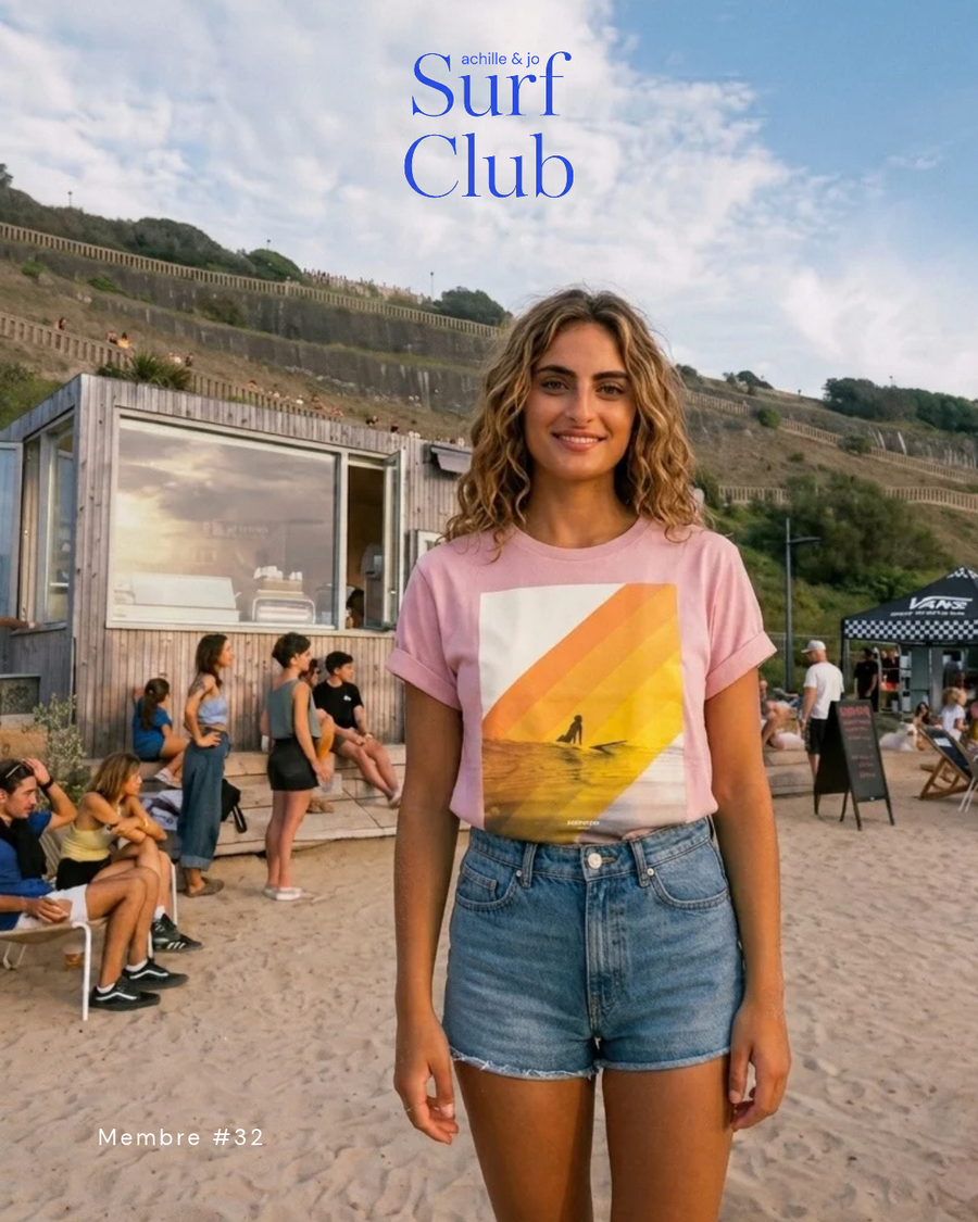Membre du Surf Club Achille & Jo en t-shirt Surfeuse rose pétale, sur la plage devant une cabane
